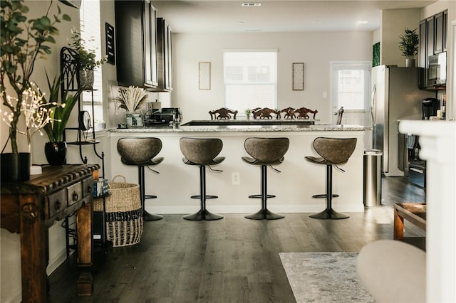 kitchen featuring white microwave, light stone counters, a kitchen breakfast bar, a peninsula, and wood finished floors