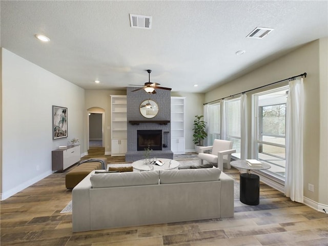 living area featuring arched walkways, visible vents, a fireplace, and light wood finished floors