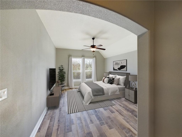 bedroom with baseboards, arched walkways, a ceiling fan, vaulted ceiling, and light wood-type flooring