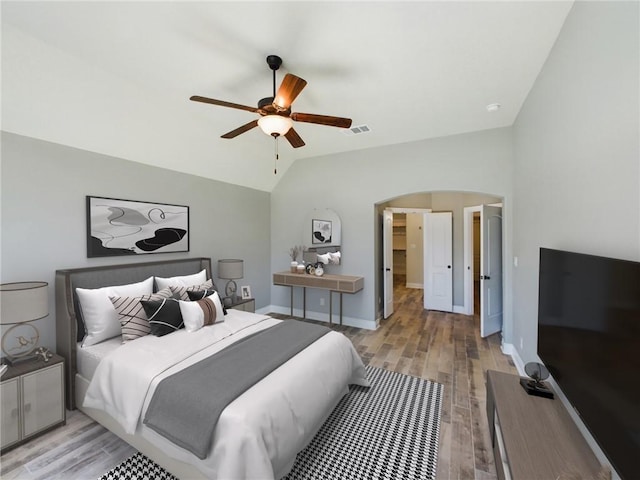 bedroom featuring light wood finished floors, visible vents, arched walkways, baseboards, and vaulted ceiling