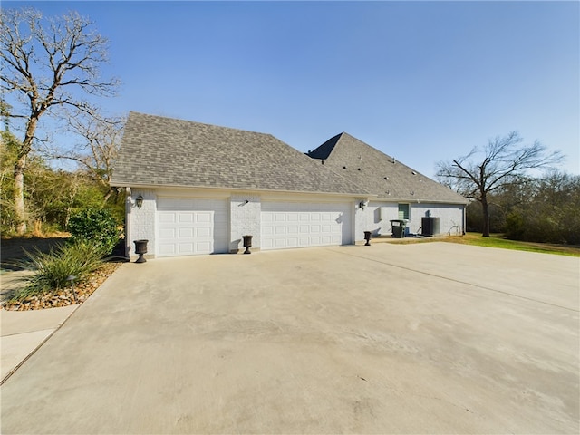 view of property exterior with a garage, roof with shingles, driveway, and central AC