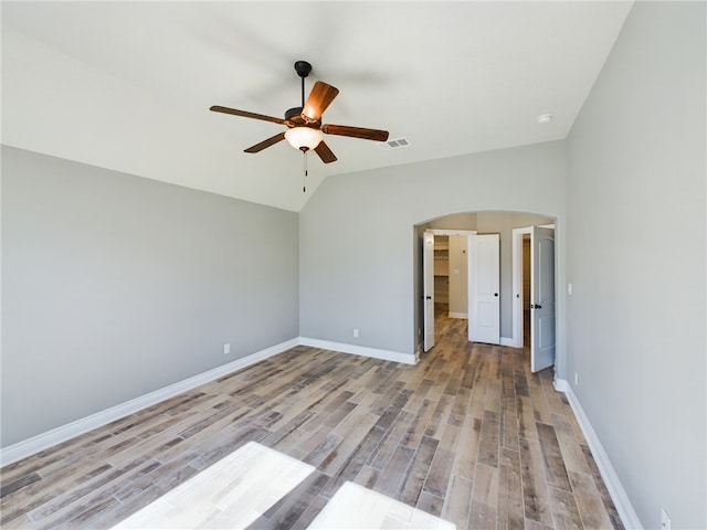 unfurnished bedroom featuring light wood-style floors, arched walkways, visible vents, and lofted ceiling