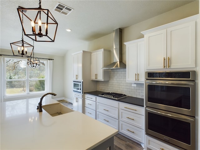 kitchen featuring visible vents, appliances with stainless steel finishes, decorative light fixtures, wall chimney range hood, and a sink