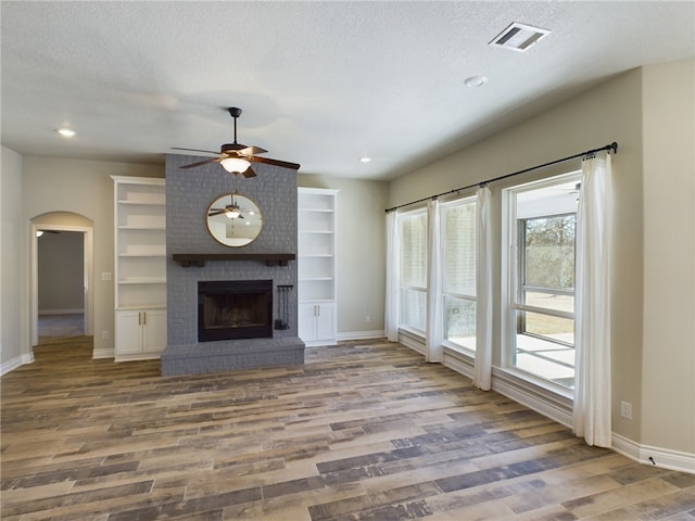 unfurnished living room with a textured ceiling, arched walkways, wood finished floors, visible vents, and a brick fireplace