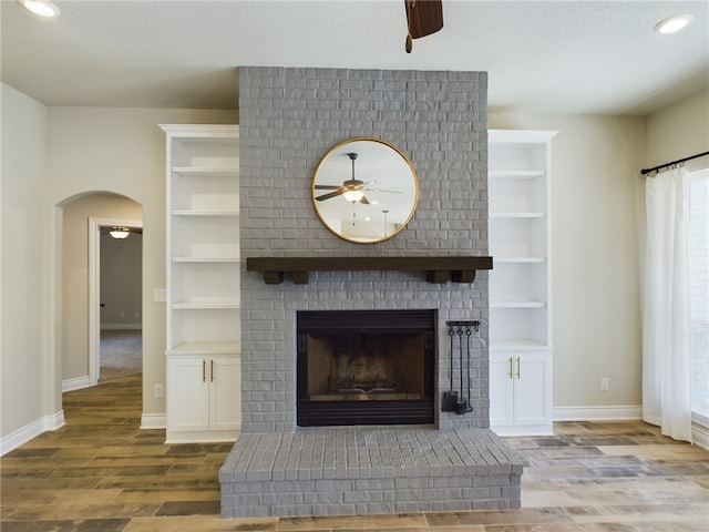 details with arched walkways, ceiling fan, a fireplace, wood finished floors, and baseboards