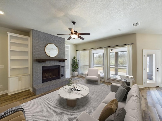 living area featuring visible vents, built in features, wood finished floors, a textured ceiling, and a brick fireplace