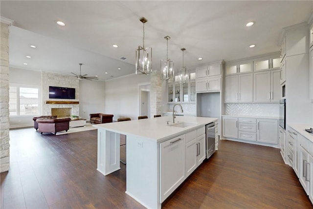 kitchen with appliances with stainless steel finishes, a kitchen island with sink, sink, white cabinets, and a stone fireplace