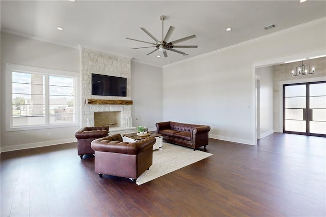 living room with crown molding, a fireplace, dark wood-type flooring, and ceiling fan with notable chandelier