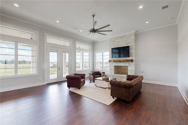 living room featuring dark hardwood / wood-style floors, a stone fireplace, ceiling fan, and ornamental molding