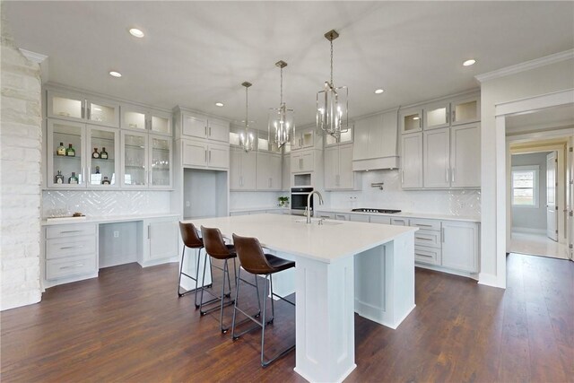 kitchen with backsplash, ornamental molding, custom range hood, dark wood-type flooring, and a spacious island