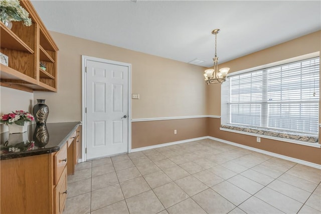 unfurnished dining area with an inviting chandelier, light tile patterned floors, and baseboards