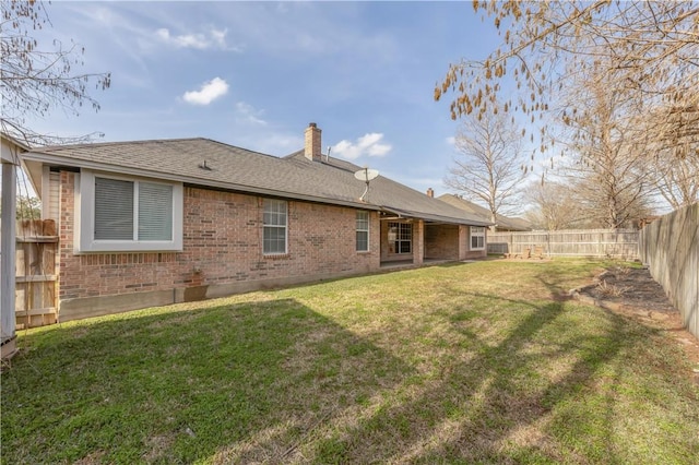 back of property featuring a yard, brick siding, a chimney, and a fenced backyard