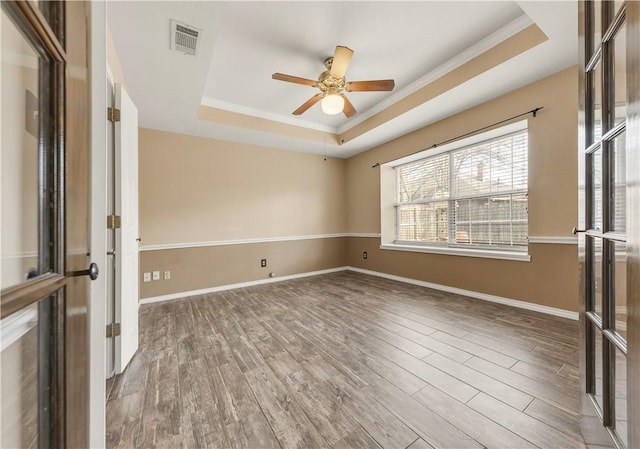 empty room with a tray ceiling, wood finished floors, and baseboards