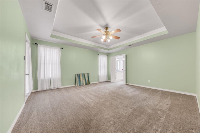 carpeted spare room featuring ornamental molding, a raised ceiling, visible vents, and baseboards