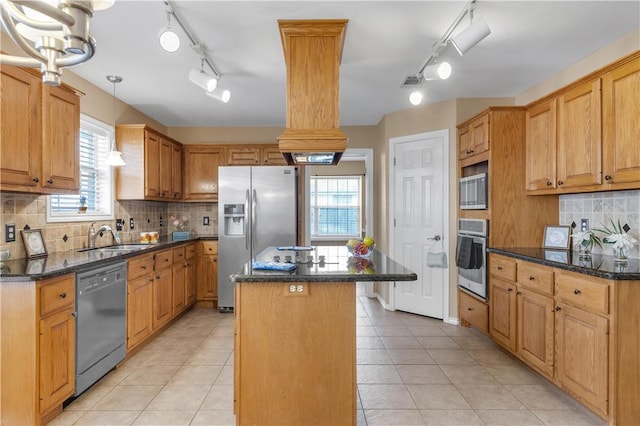 kitchen featuring a sink, hanging light fixtures, appliances with stainless steel finishes, a center island, and dark stone counters