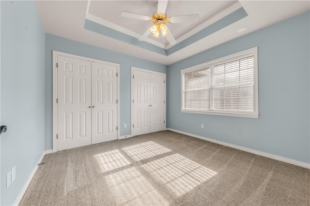 unfurnished bedroom featuring multiple closets, a raised ceiling, carpet floors, and baseboards