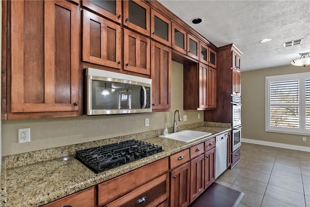 kitchen with visible vents, glass insert cabinets, stainless steel appliances, a textured ceiling, and a sink