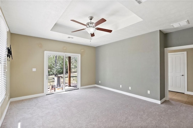 carpeted spare room featuring visible vents, ceiling fan, a raised ceiling, and baseboards