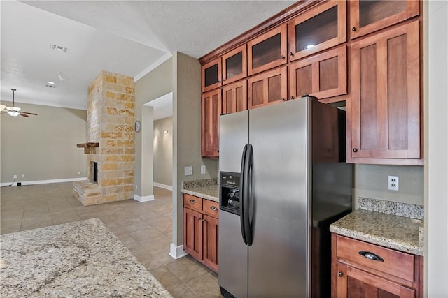 kitchen featuring light stone counters, stainless steel fridge, a large fireplace, and a ceiling fan