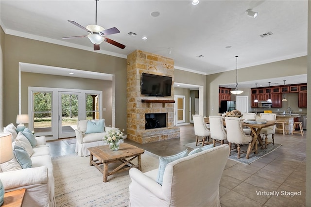 living room with visible vents, a stone fireplace, crown molding, and a ceiling fan