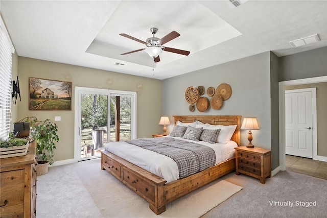 bedroom with access to exterior, visible vents, light carpet, and a tray ceiling