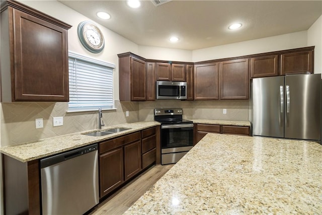 kitchen featuring light stone counters, a sink, dark brown cabinetry, decorative backsplash, and stainless steel appliances