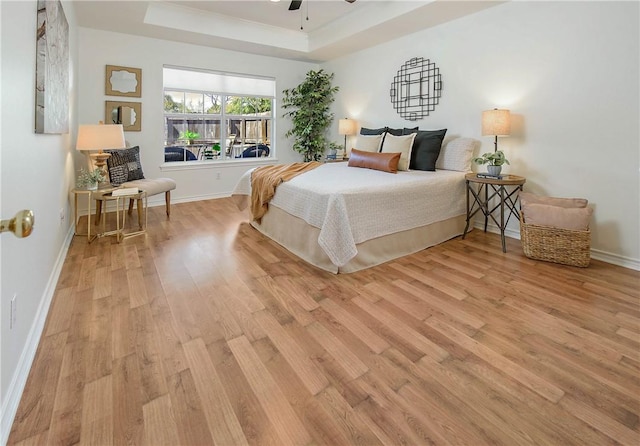 bedroom with a raised ceiling, baseboards, light wood-type flooring, and ceiling fan