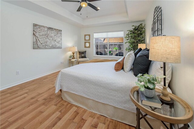 bedroom featuring a ceiling fan, a tray ceiling, wood finished floors, and baseboards