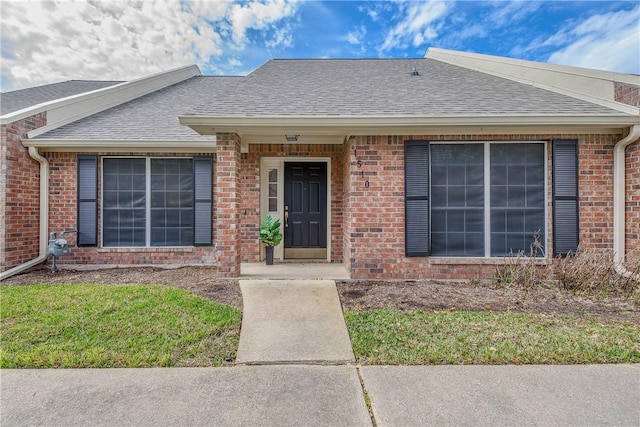 doorway to property with brick siding and roof with shingles