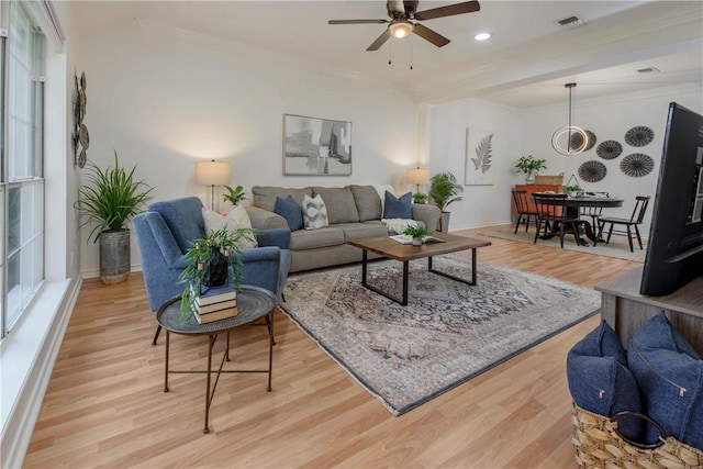 living room with baseboards, visible vents, light wood finished floors, and ornamental molding