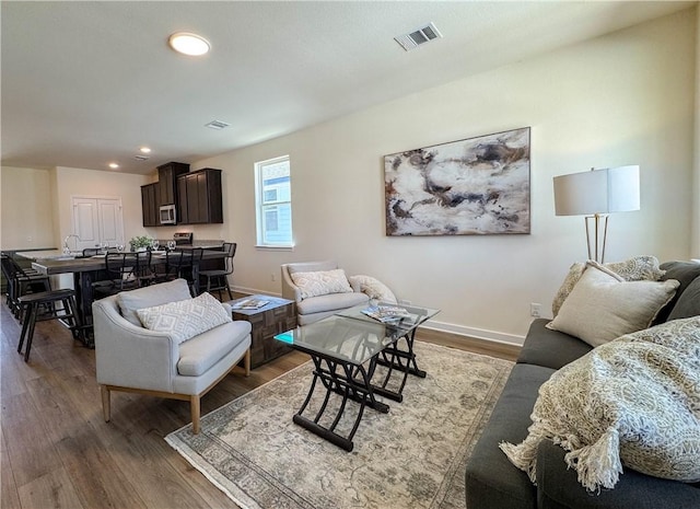 living area with recessed lighting, wood finished floors, visible vents, and baseboards