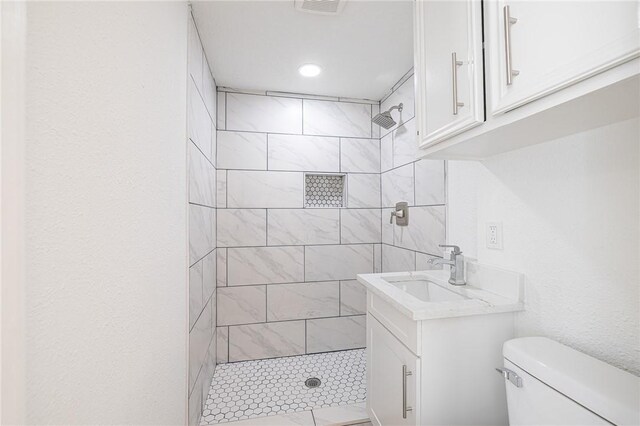 bathroom with tiled shower, vanity, and toilet