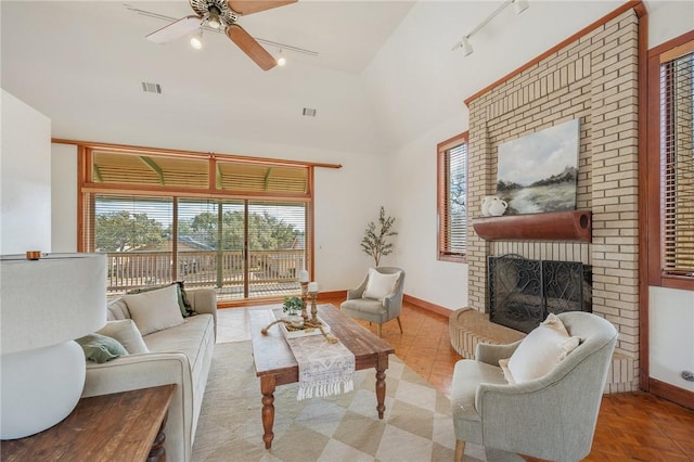 living room featuring high vaulted ceiling, rail lighting, ceiling fan, light parquet flooring, and a brick fireplace