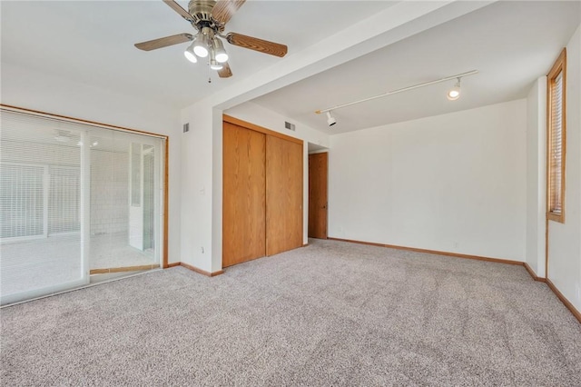 unfurnished bedroom with ceiling fan, a closet, rail lighting, and light carpet