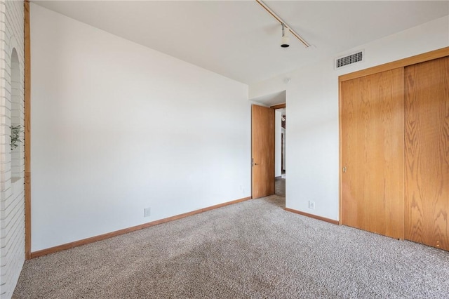 unfurnished bedroom with light colored carpet, rail lighting, and a closet