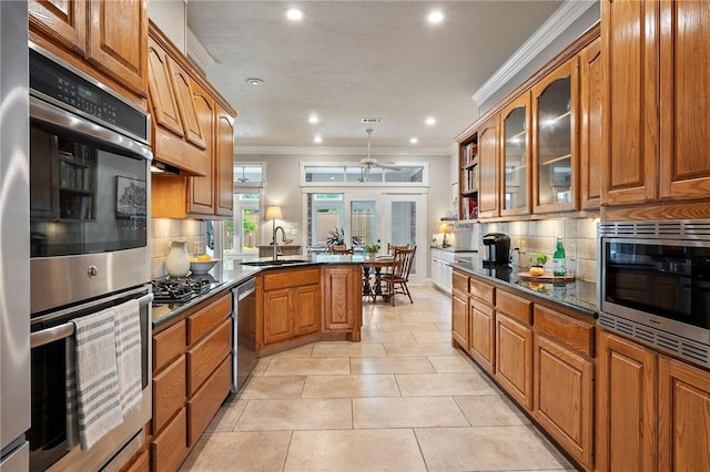 kitchen with brown cabinetry, a peninsula, ceiling fan, a sink, and appliances with stainless steel finishes