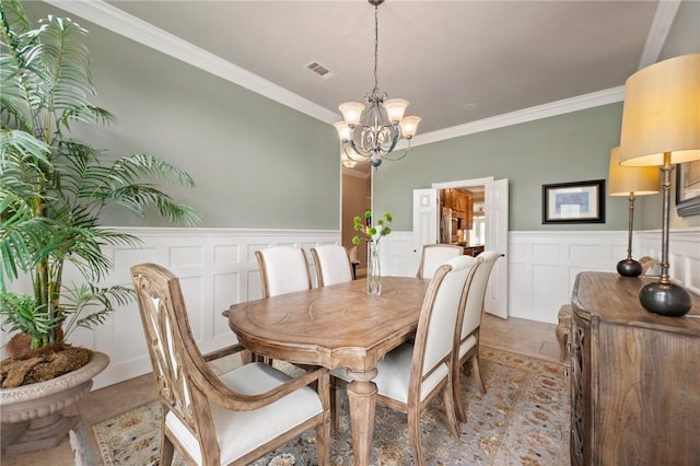 dining space with visible vents, crown molding, a wainscoted wall, an inviting chandelier, and a decorative wall