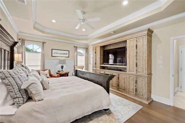 bedroom with crown molding, wood finished floors, and a raised ceiling