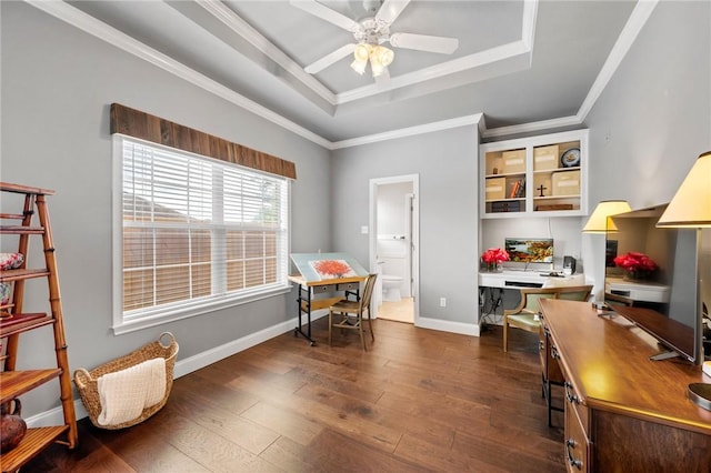 home office featuring ceiling fan, baseboards, a raised ceiling, dark wood-style floors, and ornamental molding