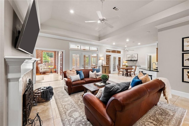 living area featuring a raised ceiling, a fireplace, a ceiling fan, and visible vents