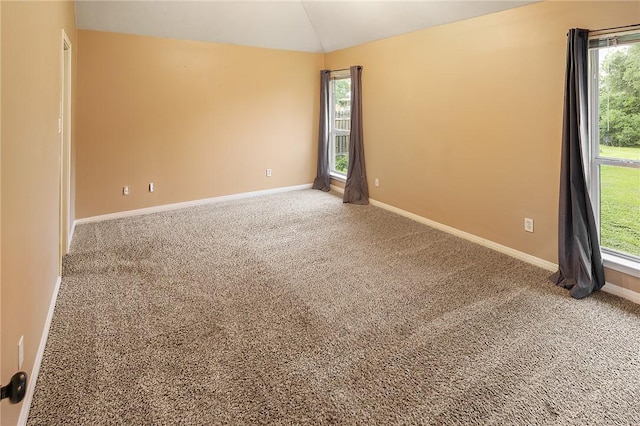 carpeted spare room featuring vaulted ceiling, plenty of natural light, and baseboards
