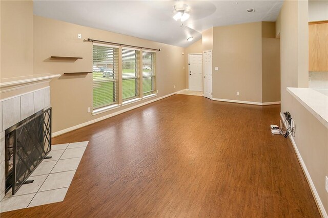 unfurnished living room featuring a tile fireplace, lofted ceiling, wood finished floors, baseboards, and ceiling fan