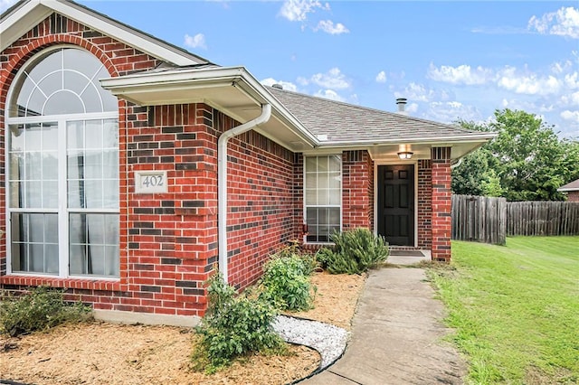 doorway to property featuring brick siding and roof with shingles