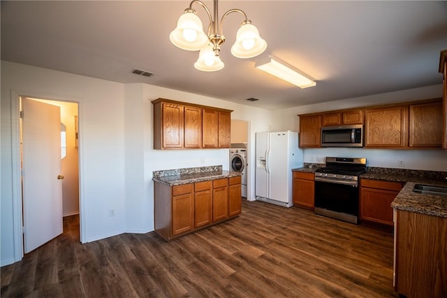 kitchen with pendant lighting, appliances with stainless steel finishes, washer / clothes dryer, dark wood-type flooring, and a chandelier