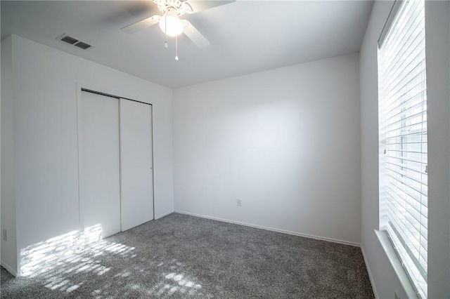 unfurnished bedroom featuring ceiling fan, a closet, dark colored carpet, and multiple windows