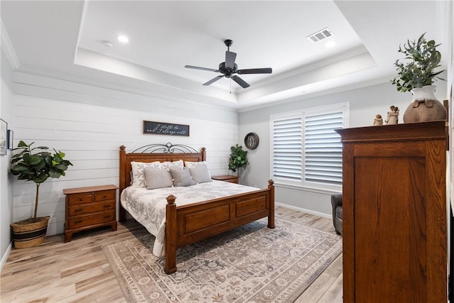 bedroom featuring ornamental molding, a raised ceiling, ceiling fan, light hardwood / wood-style floors, and wood walls