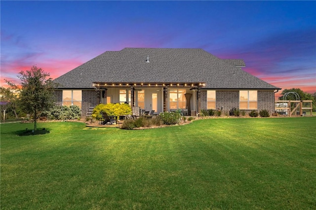 back house at dusk featuring a lawn