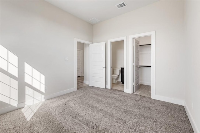 unfurnished bedroom with ensuite bathroom, a spacious closet, light carpet, and a closet