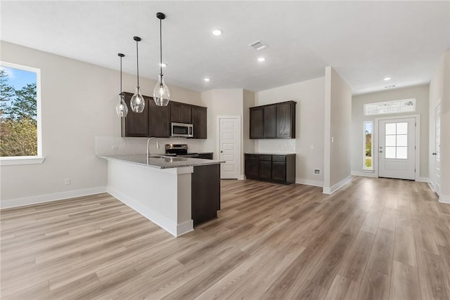 kitchen with kitchen peninsula, appliances with stainless steel finishes, decorative backsplash, light stone countertops, and hanging light fixtures