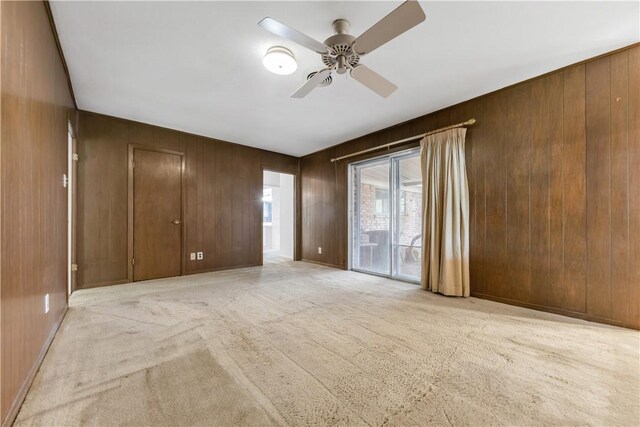unfurnished bedroom with access to exterior, carpet floors, wood walls, baseboards, and ceiling fan